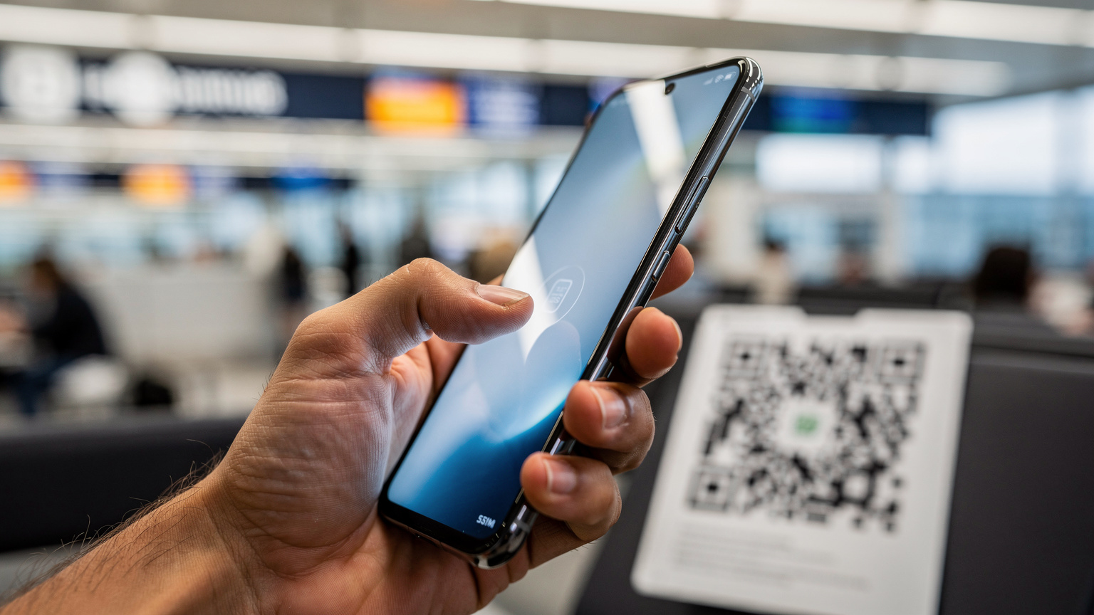 Uma mão segurando um smartphone, com o polegar tocando a tela para instalar um eSIM via QR code, em um ambiente de aeroporto movimentado, simbolizando a facilidade da ativação.