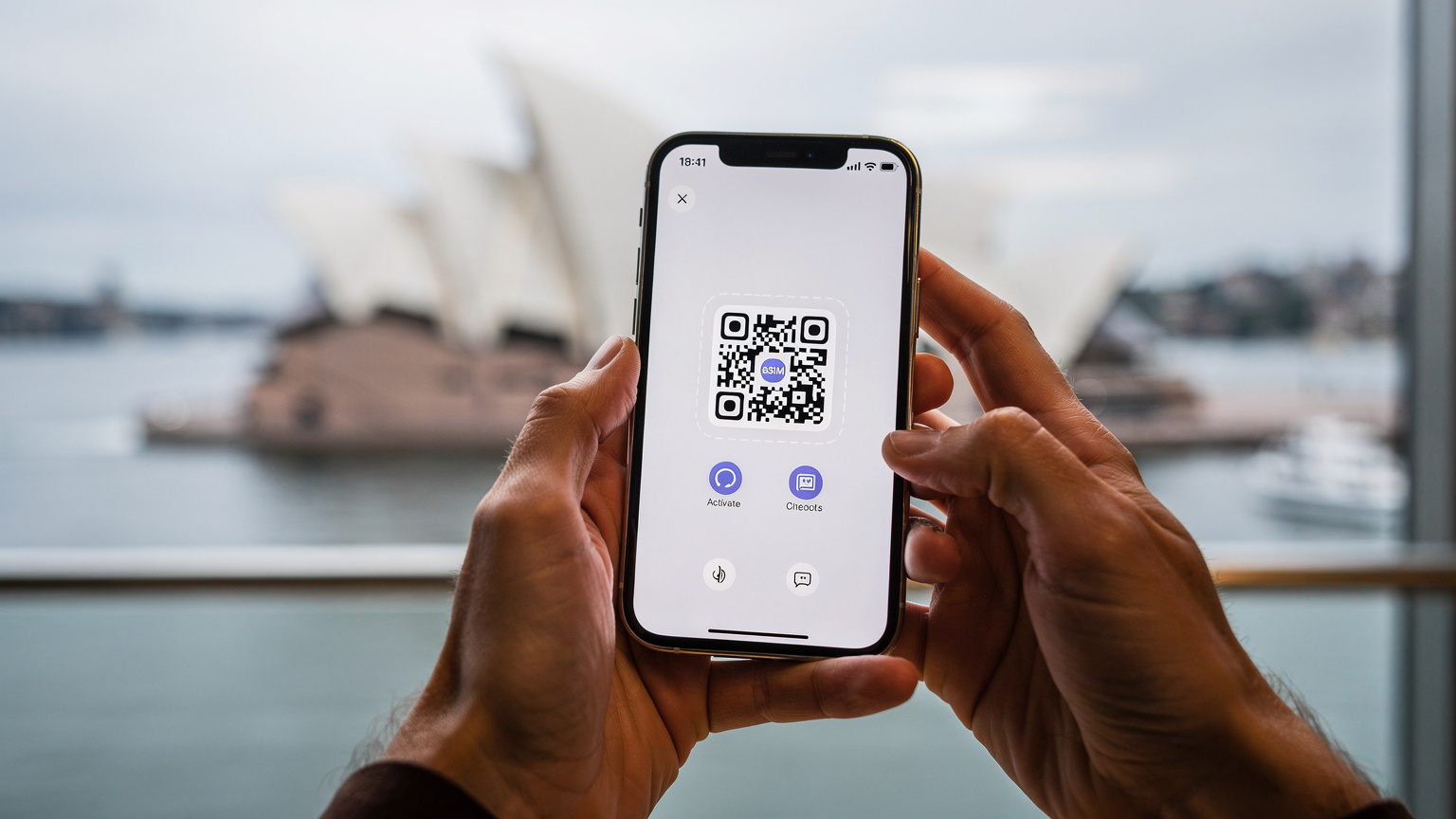 Primer plano de unas manos sosteniendo un iPhone, mostrando el proceso de escaneo de un código QR para activar una eSIM, con la Ópera de Sídney y el puerto de fondo desenfocados.
