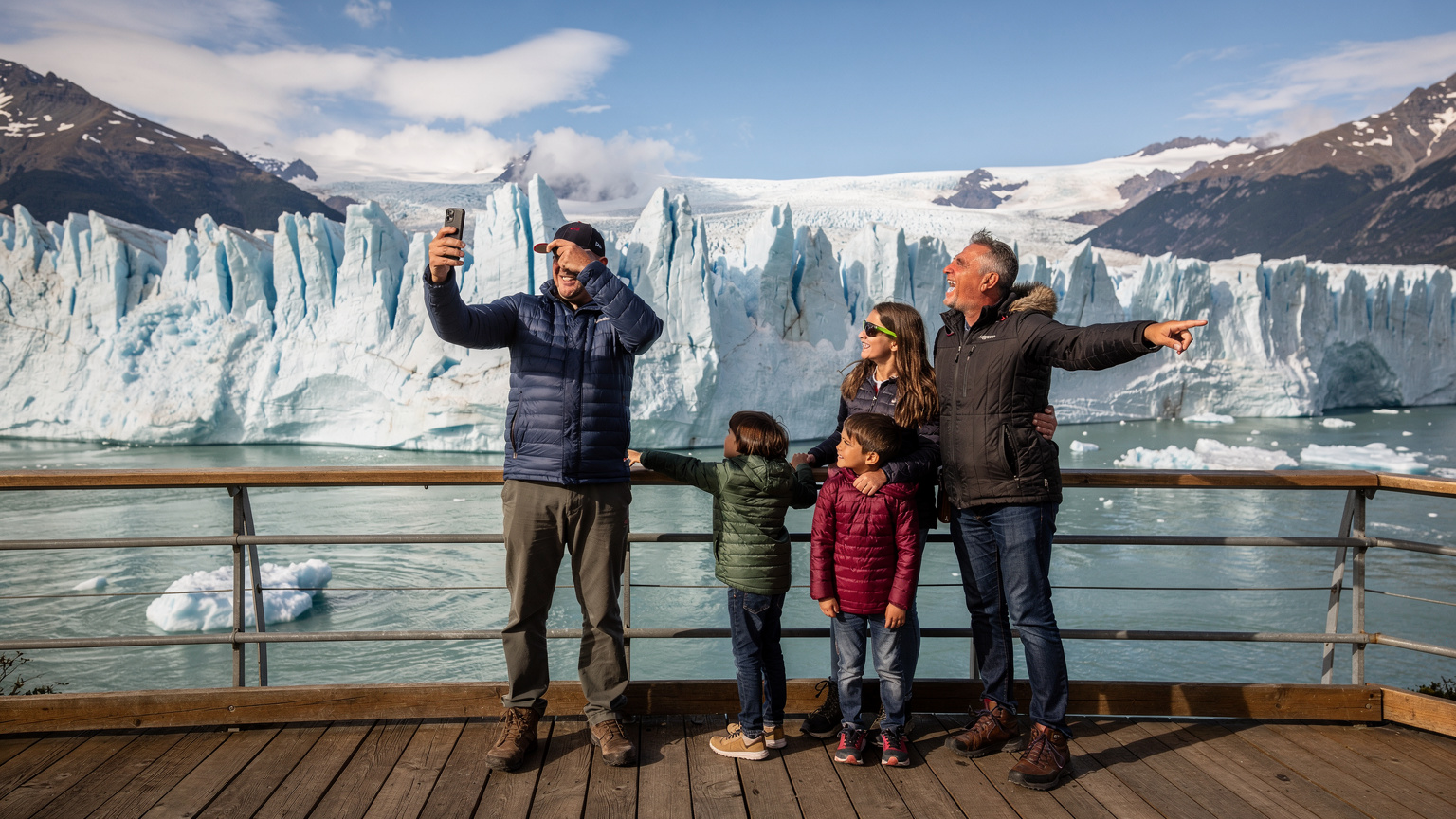 Une famille en Patagonie argentine, avec le glacier Perito Moreno en arrière-plan, vérifiant la connectivité de leurs appareils avant de s'engager dans une zone potentiellement sans réseau.