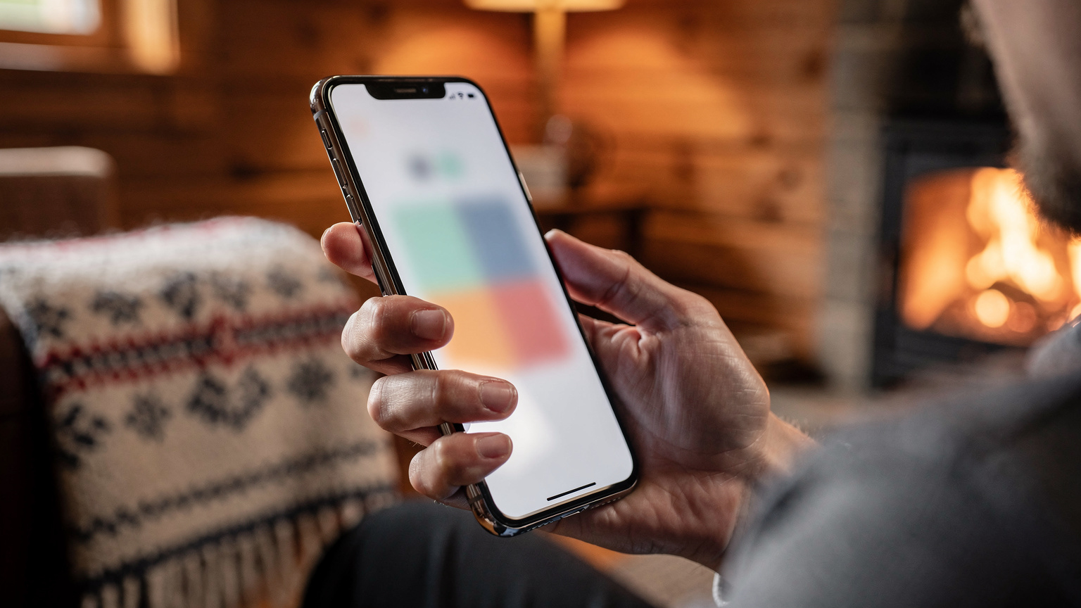 En nærbillede af en hånd, der holder en smartphone og viser en indstillingsmenu for mobilnetværk, hvor en eSIM-profil er valgt, mod en sløret baggrund af en hyggelig norsk hytteindretning.
