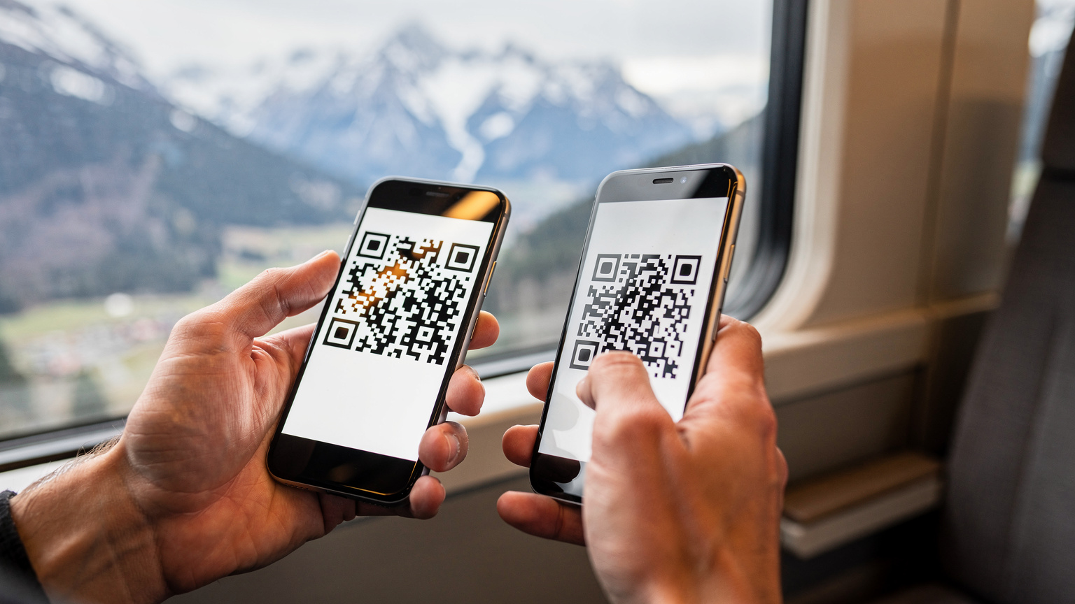 Gros plan sur des mains tenant un smartphone et scannant un QR code pour activer une eSIM, avec un arrière-plan flou de montagnes enneigées et un ciel bleu.