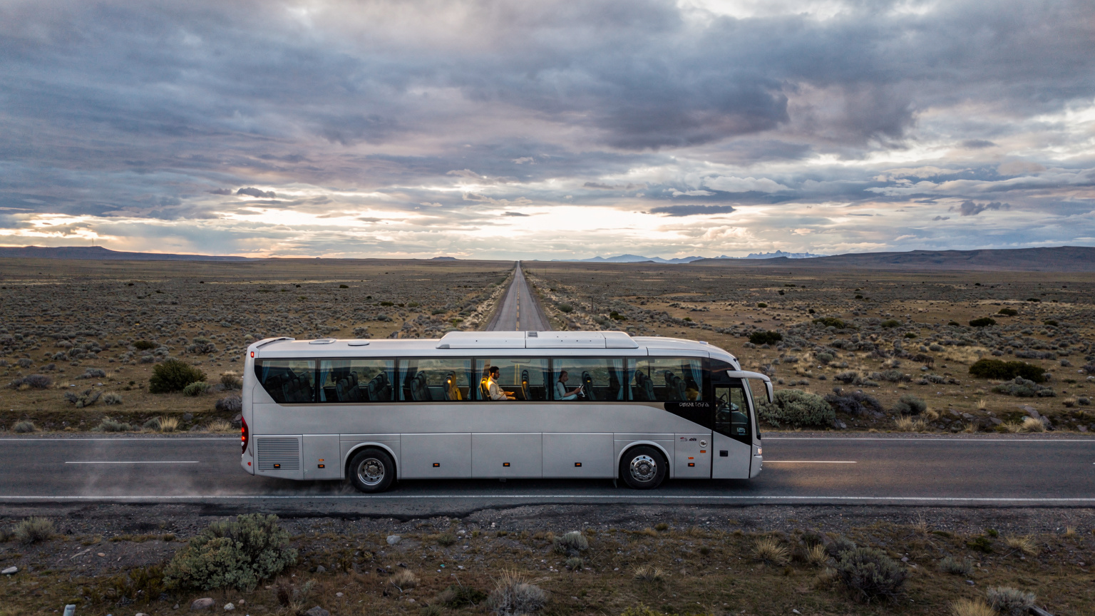 Un autobús de larga distancia atraviesa una carretera solitaria en la vasta estepa patagónica, con un viajero en el asiento de la ventana revisando su teléfono para confirmar la conectividad transfronteriza.